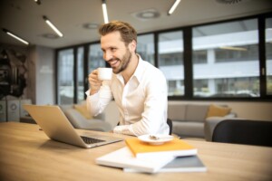 Young professional man smiling and holding a coffee cup, in an online conversation worth having certification course